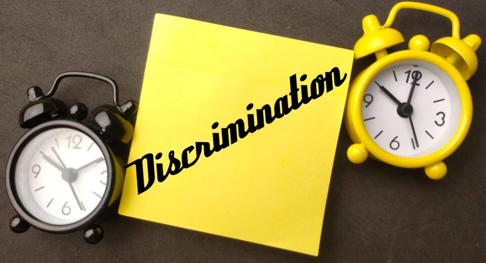 Alarm clock and sticky note with the word Discrimination on black background.