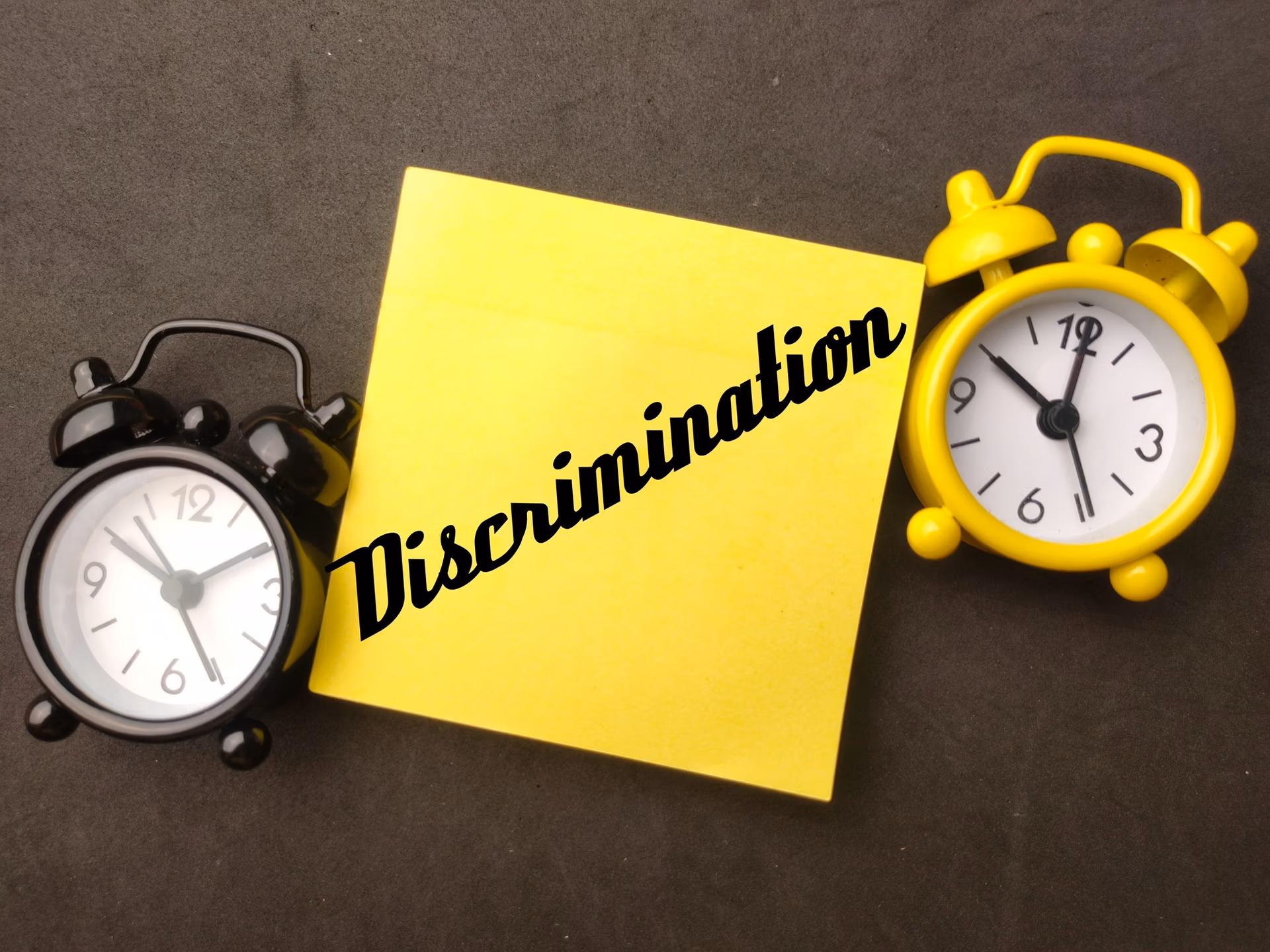 Alarm clock and sticky note with the word Discrimination on black background.