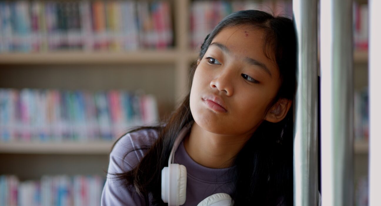 An Asian woman sits on a railing, her face showing stress, boredom, and disappointment.