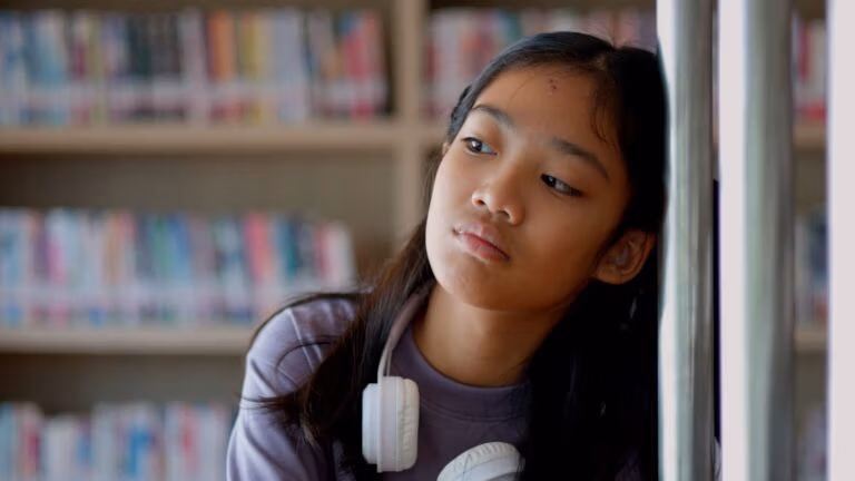 An Asian woman sits on a railing, her face showing stress, boredom, and disappointment.