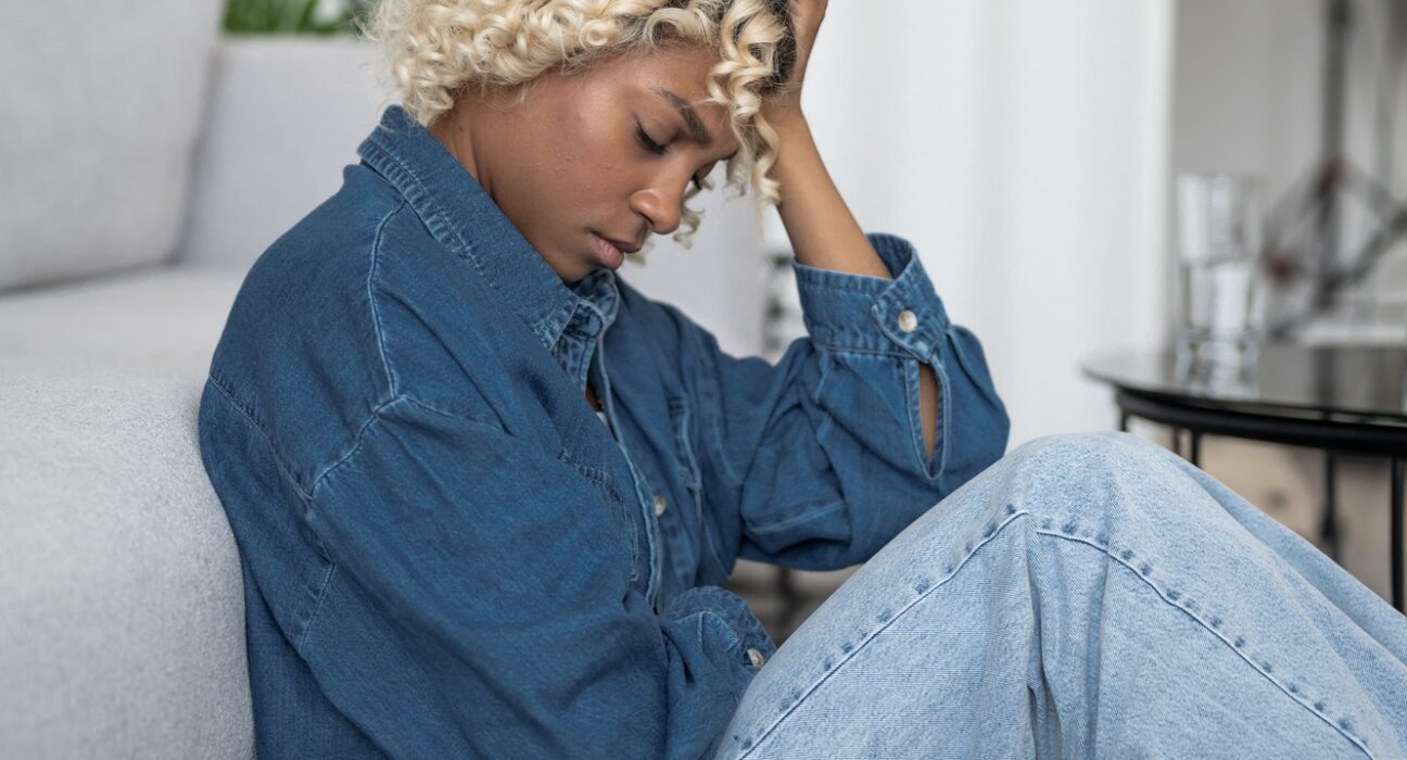 burnout,devastated and depressed young woman sits near couch with her head in her hands. Mental