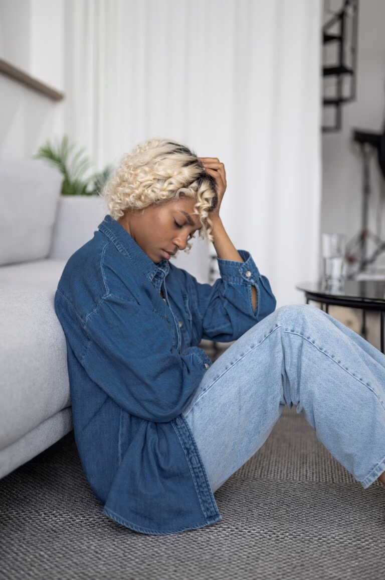 burnout,devastated and depressed young woman sits near couch with her head in her hands. Mental