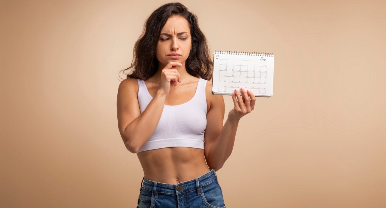 Confused millennial woman with calendar on beige background