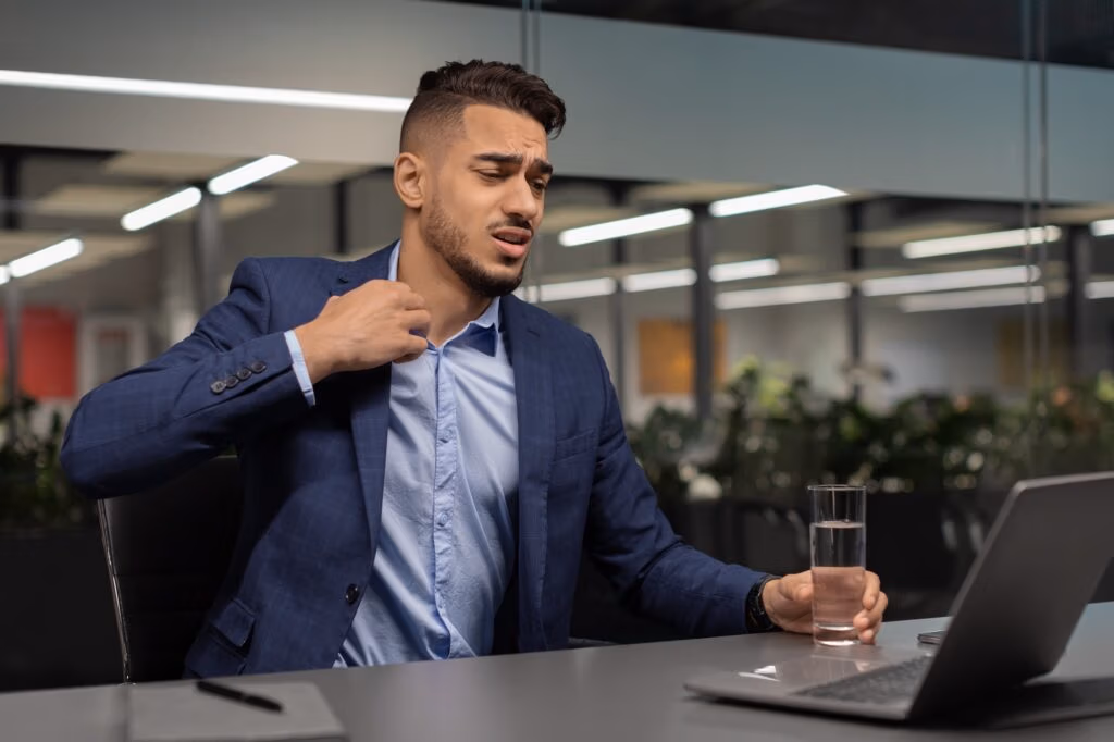 Distressed middle eastern businessman looking at notebook screen, unbuttoning shirt