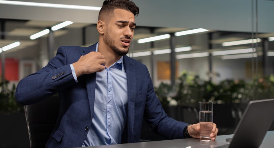 Distressed middle eastern businessman looking at notebook screen, unbuttoning shirt
