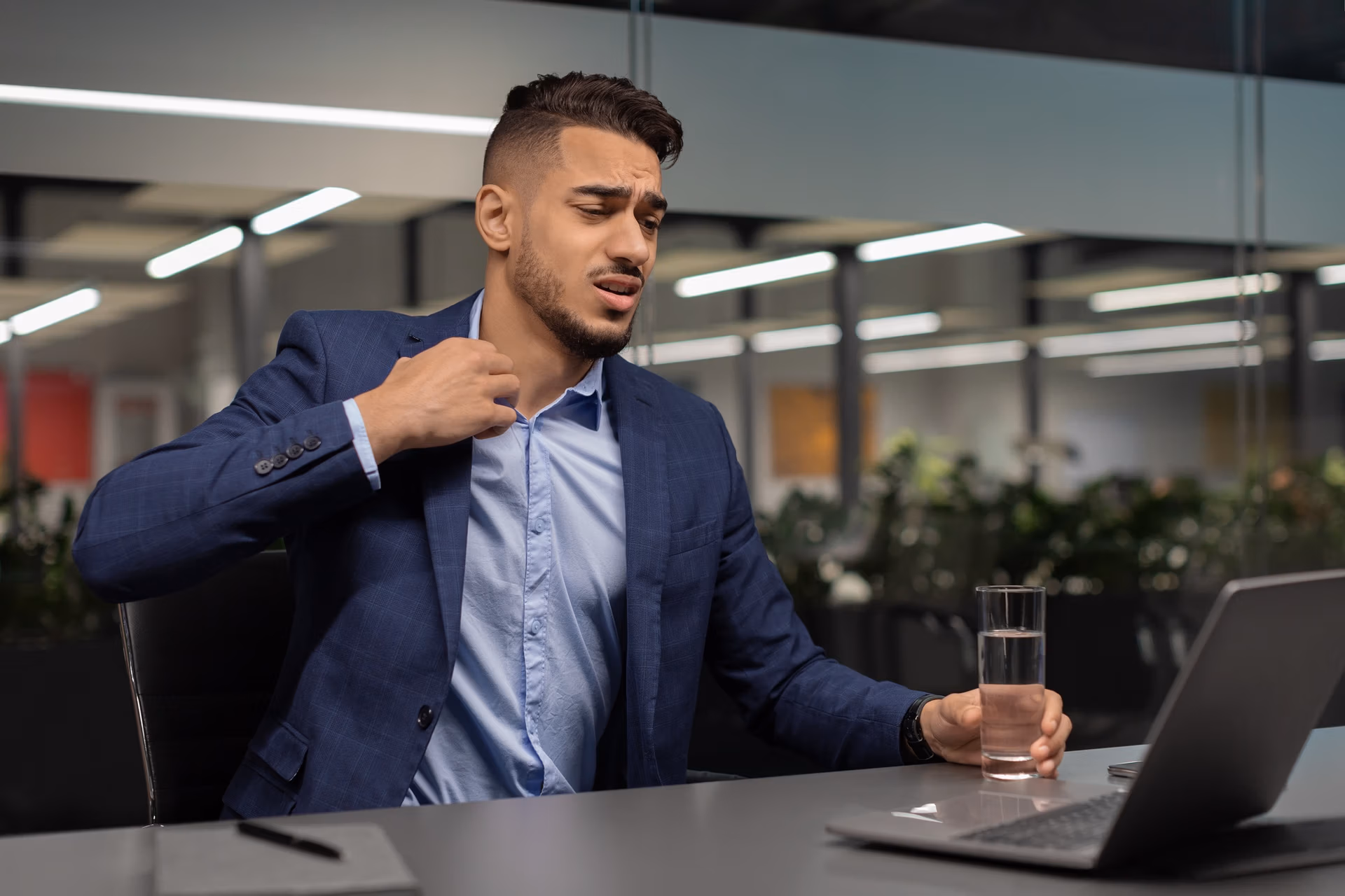Distressed middle eastern businessman looking at notebook screen, unbuttoning shirt