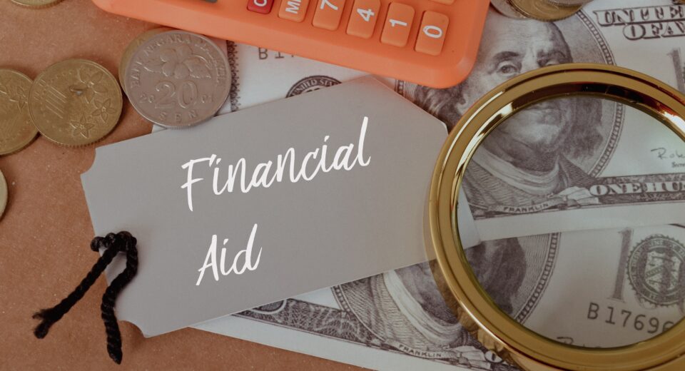 Magnifying glass, calculator and money with text FINANCIAL AID.