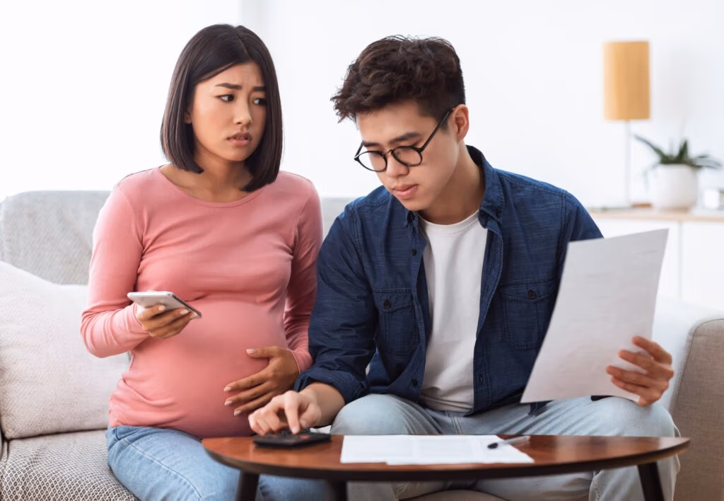 Unhappy Chinese Spouses Calculating Bills Sitting On Sofa At Home