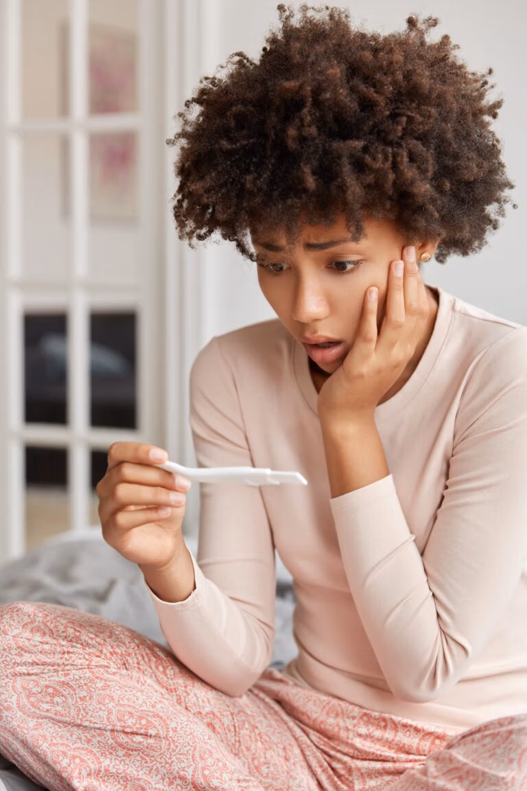 Vertical shot of stupefied woman with Afro haircut, checks positive result on pregnancy test, finds