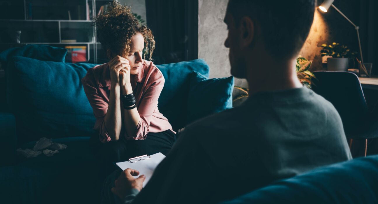 woman in pink blouse gets emotional support from professional psychologist sitting on sofa