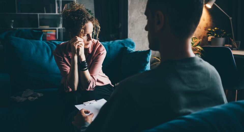 woman in pink blouse gets emotional support from professional psychologist sitting on sofa