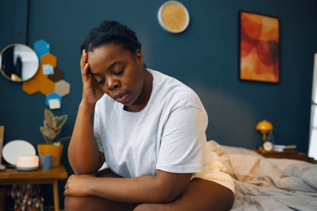 Woman Sitting in Bedroom Holding Head with Hand