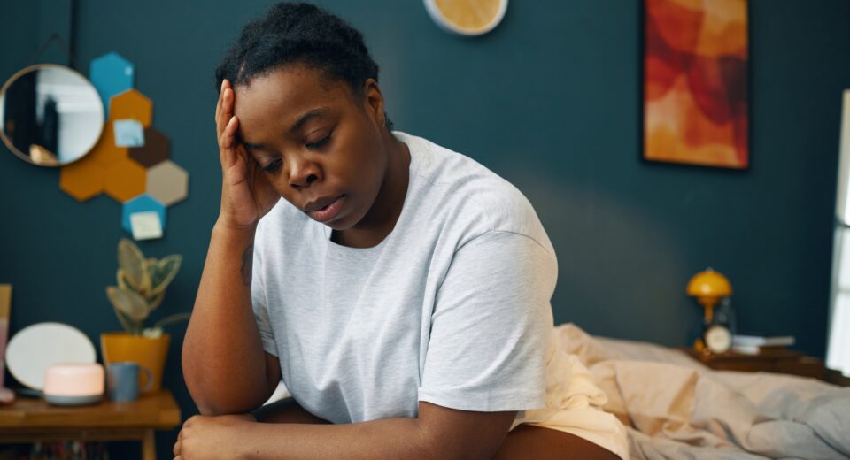 Woman Sitting in Bedroom Holding Head with Hand