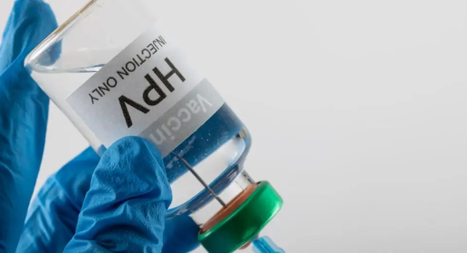 Composition of doctor's gloved hands filling syringe from hpv vaccine vial, on white with copy space