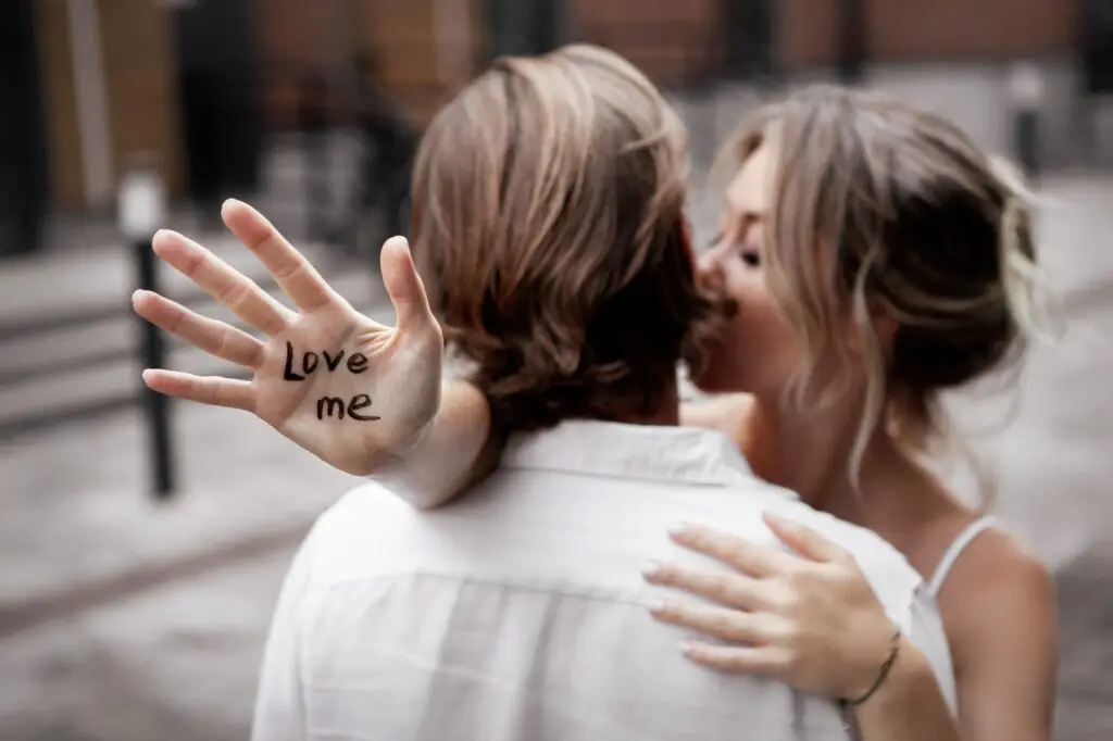 Сlose up hand with text "love me". Blurred background of young couple in love