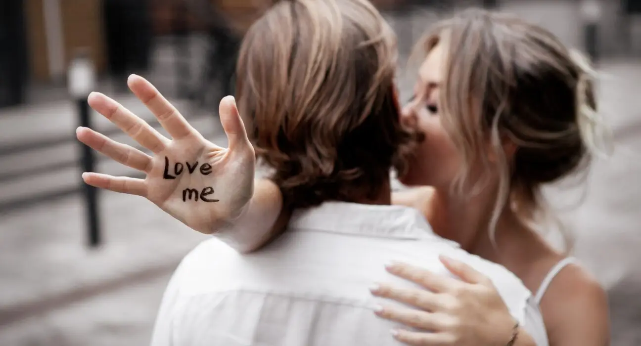 Сlose up hand with text "love me". Blurred background of young couple in love