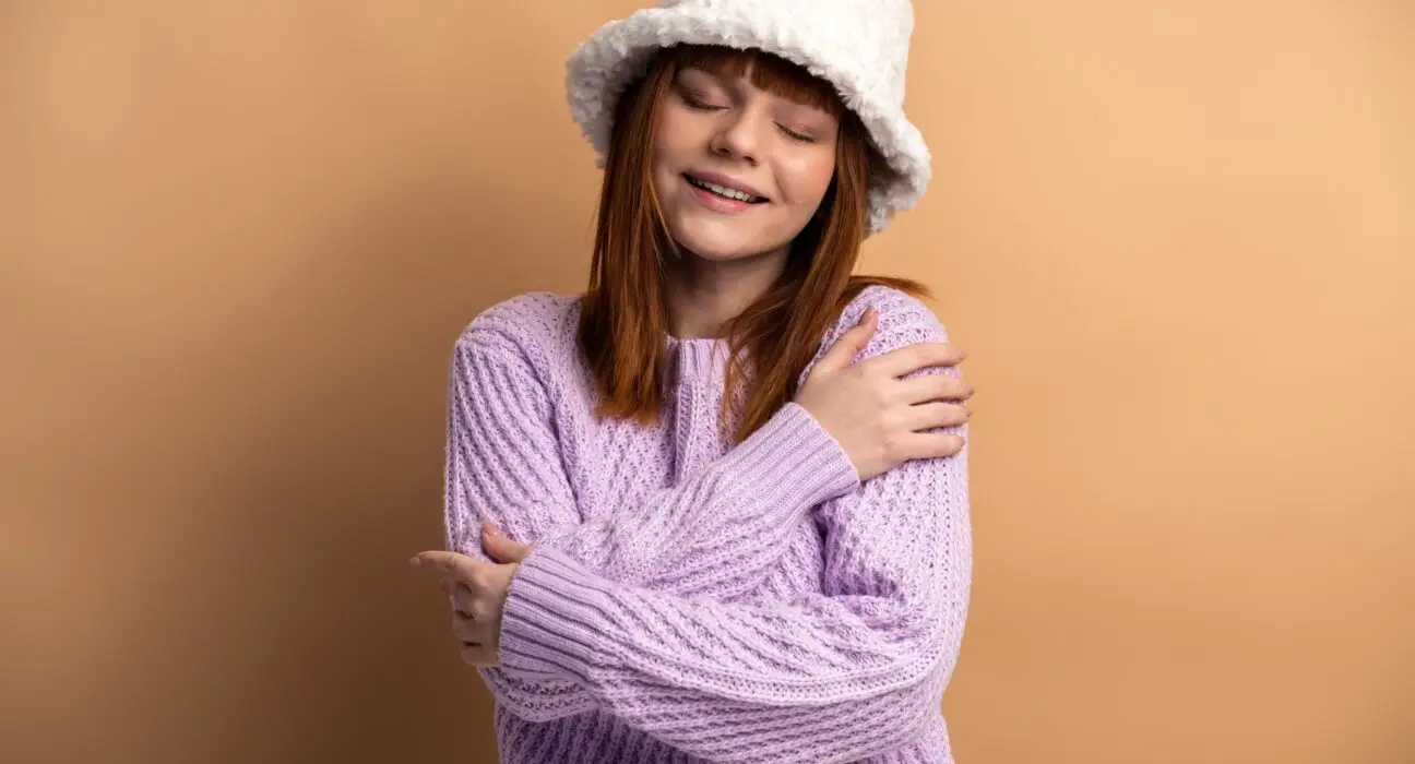 Pleased satisfied ginger girl hugging herself and smiling, feeling comfortable and fulfilled