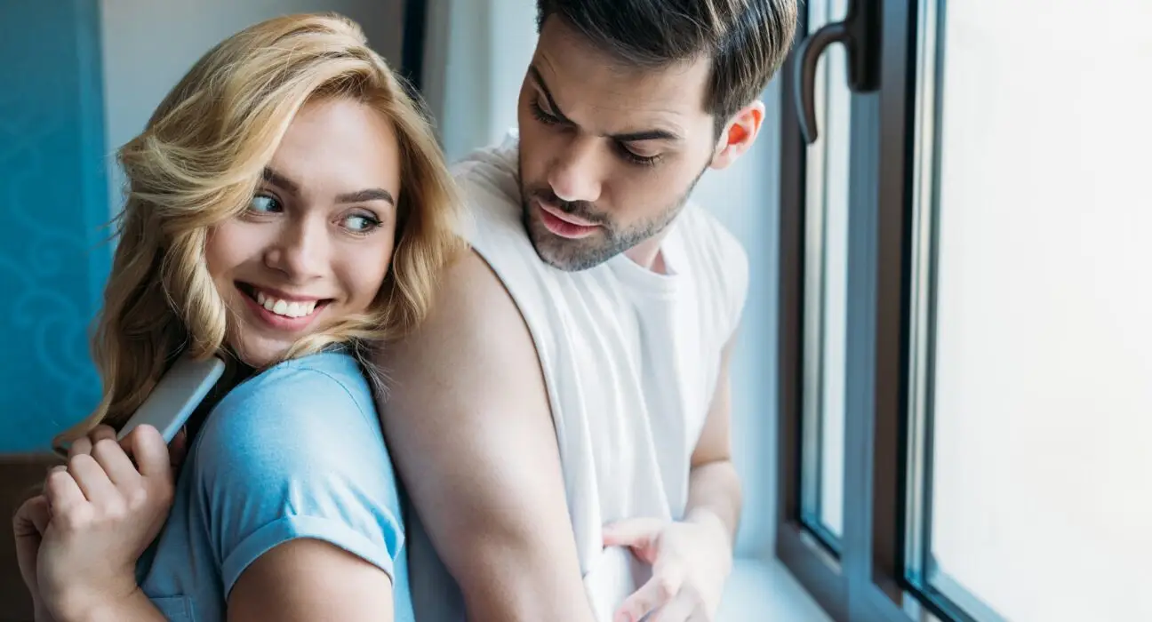 smiling couple hiding smartphones from each other