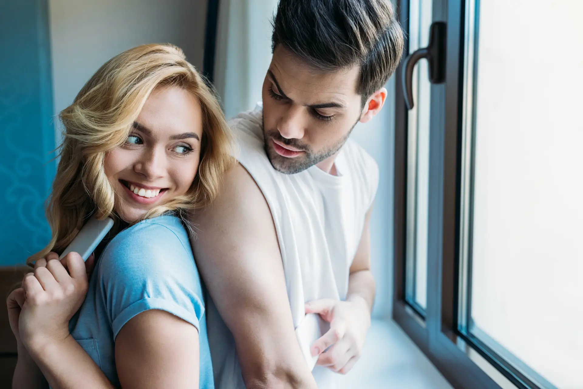 smiling couple hiding smartphones from each other