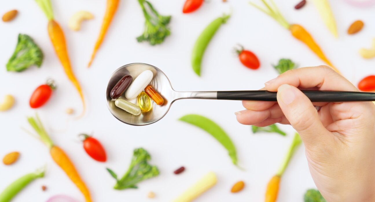 Top view close up of spoon full of vitamins and protein capsules with colorful vegetables background