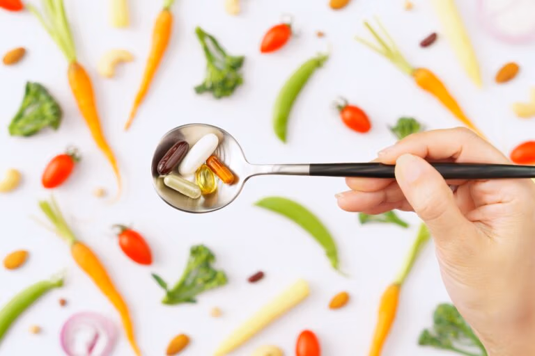 Top view close up of spoon full of vitamins and protein capsules with colorful vegetables background