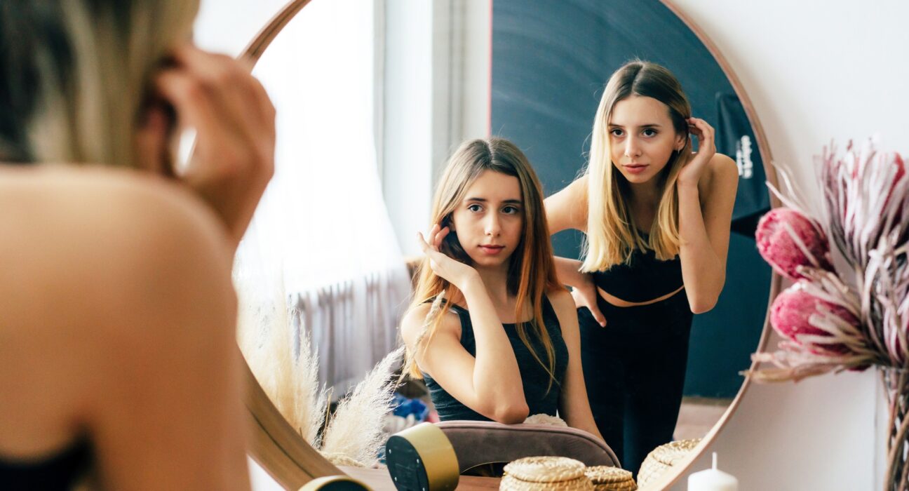 Two beautiful teenage girls look at their reflection in the mirror. Young narcissistic women.