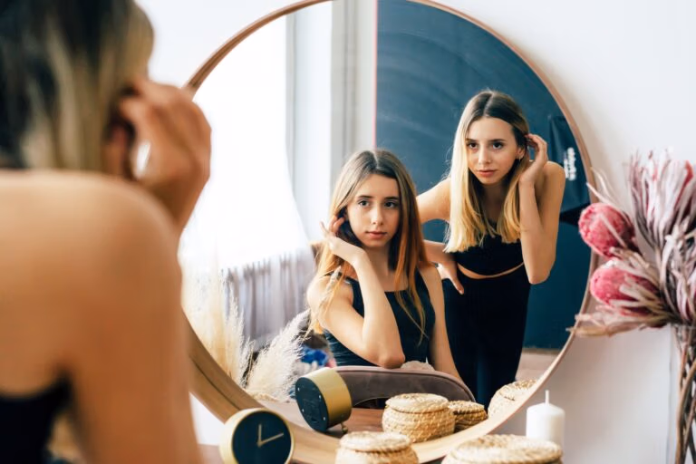 Two beautiful teenage girls look at their reflection in the mirror. Young narcissistic women.