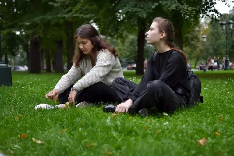 Two young women are sitting on the lawn in the park talking, sharing experiences and victories.