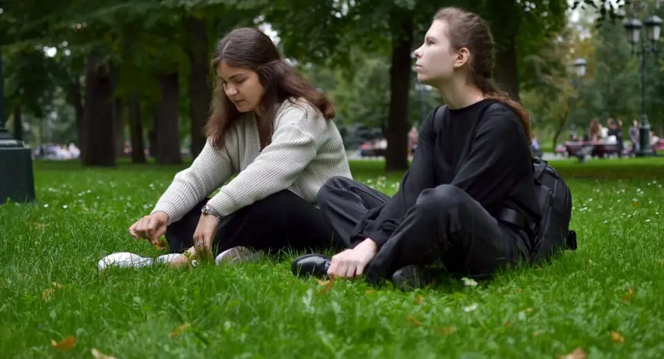 Two young women are sitting on the lawn in the park talking, sharing experiences and victories.
