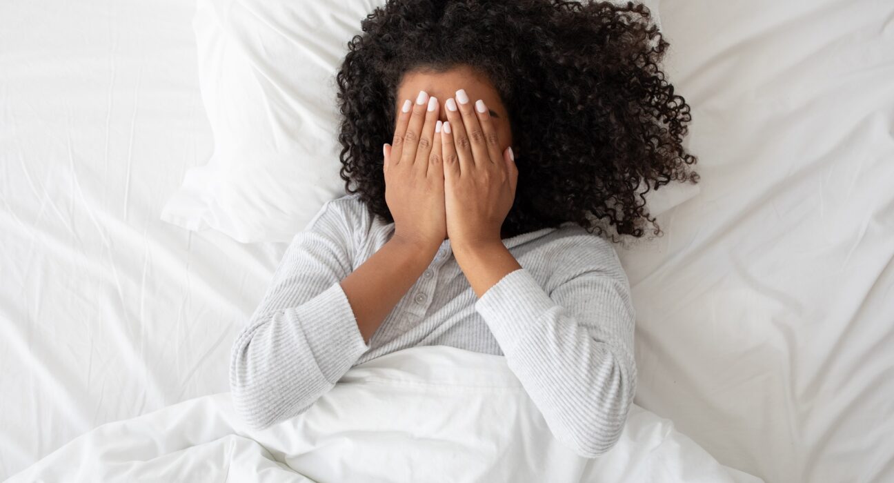 Woman Laying in Bed Covering Face With Hands