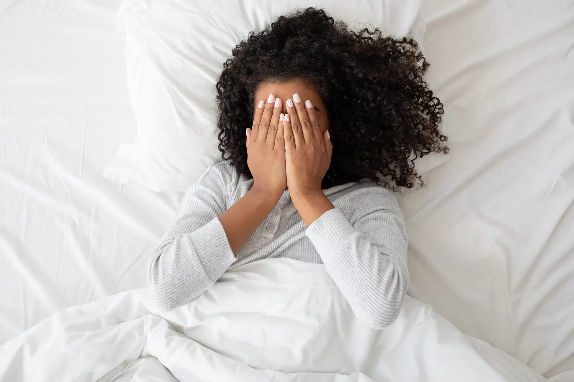 Woman Laying in Bed Covering Face With Hands