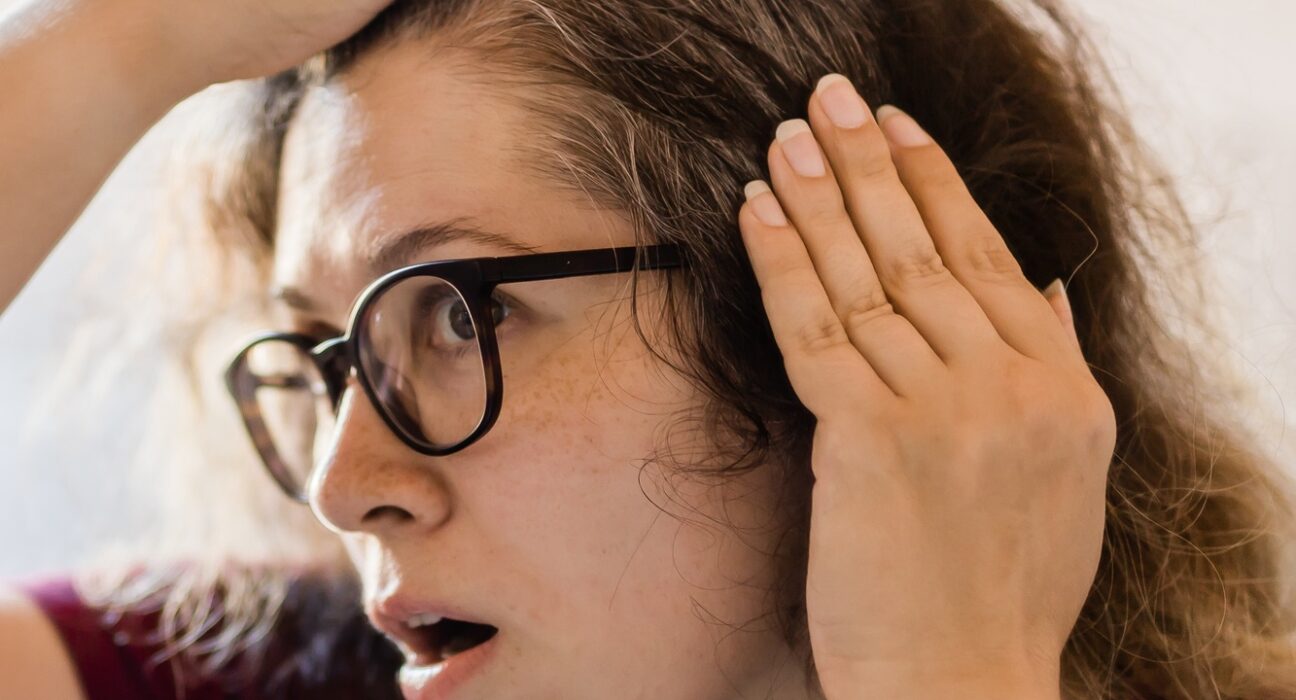 Woman Looking for Gray Hair in the Mirror. Young woman scared of premature aging signs