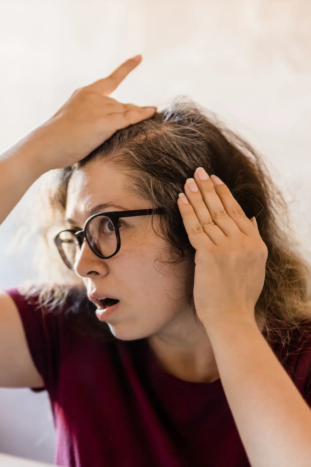 Woman Looking for Gray Hair in the Mirror. Young woman scared of premature aging signs