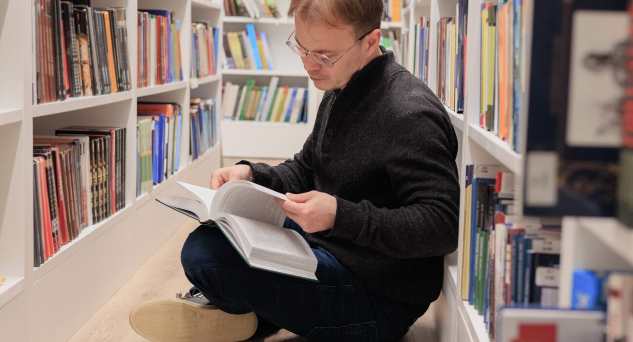 man is sitting on floor in library and reading book. education at university campus