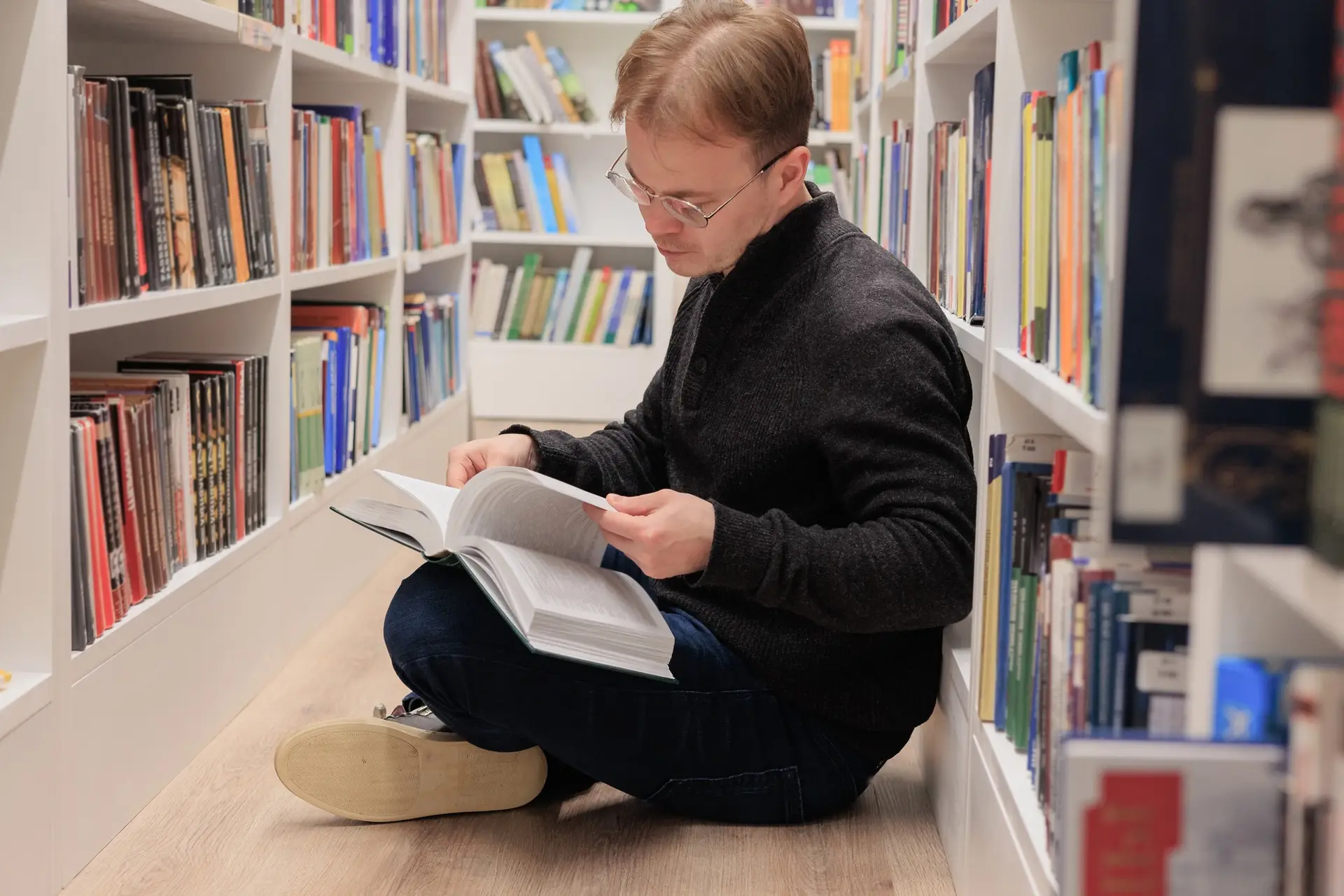 man is sitting on floor in library and reading book. education at university campus