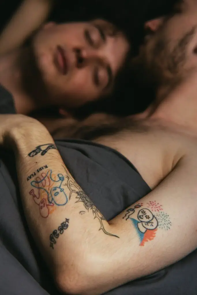 tattooed man lying in bed with man