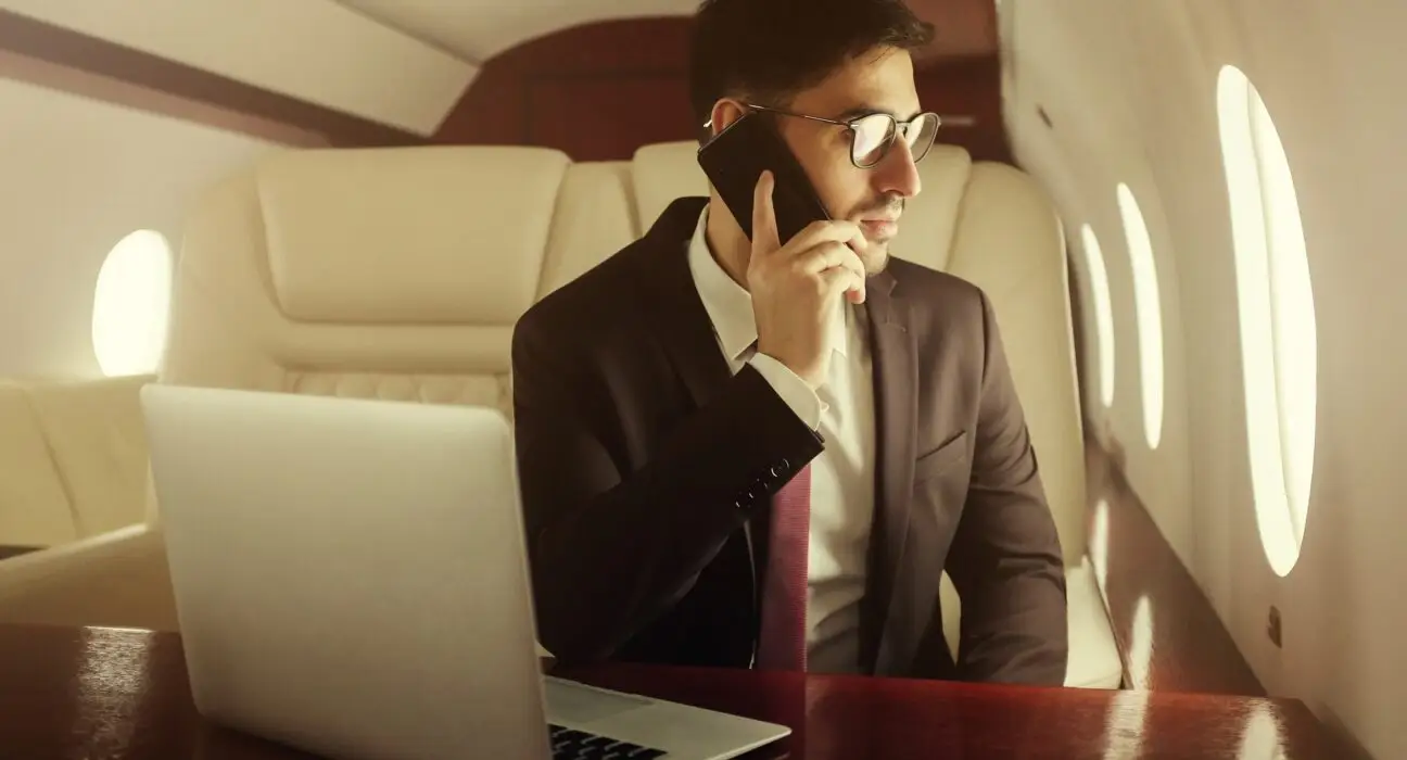 Rich man travelling first class, sitting in leather armchair at table, talking on phone