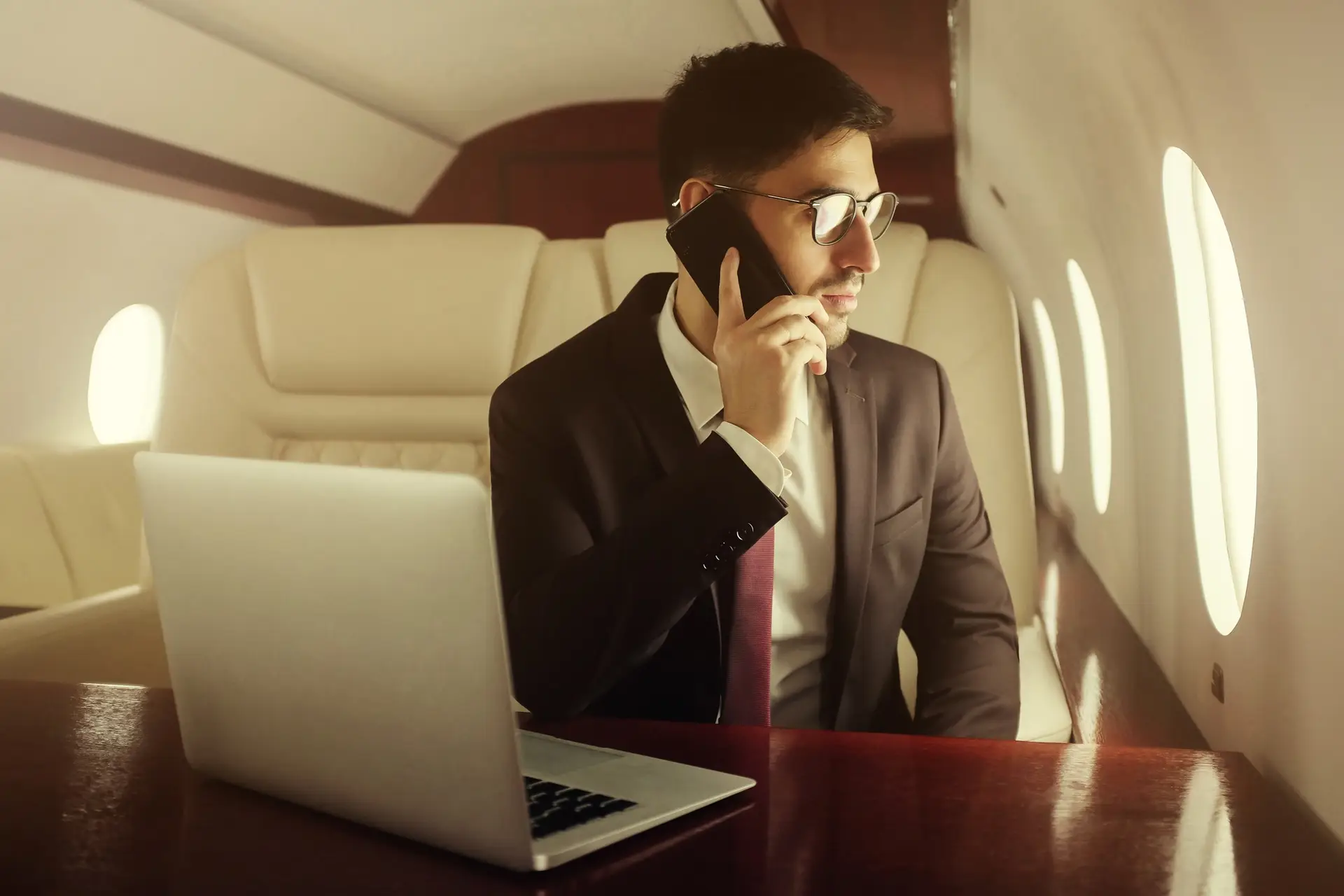 Rich man travelling first class, sitting in leather armchair at table, talking on phone